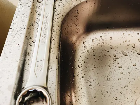 Llave de gasfitero sobre un lavadero de acero con gotas de agua